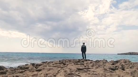 时尚英俊的新郎独自站在岩石海滩上看着大海塞浦路斯视频的预览图