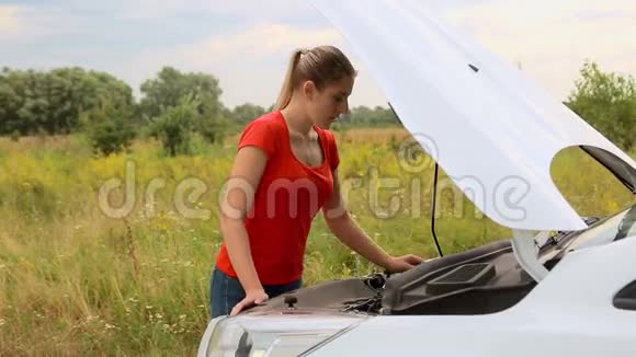 一位年轻女子在田野里看着故障车的引擎视频的预览图