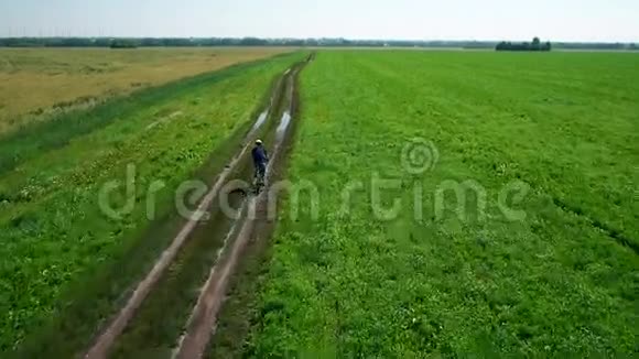 年轻人骑自行车在乡村公路上穿过绿色和黄色的田野视频的预览图