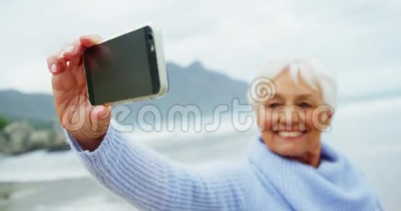 在沙滩上拍手机的高级女性视频的预览图