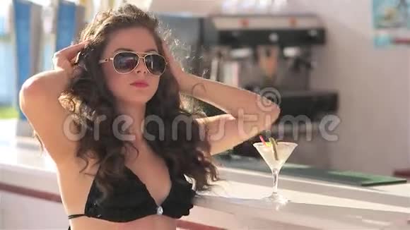 年轻美丽的女孩在海滩酒吧穿比基尼鸡尾酒在日落时喝酒和摆姿势视频的预览图