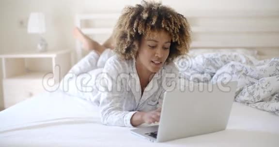 女人在家的床上看手提电脑视频的预览图