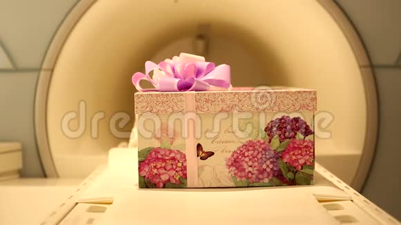 一个漂亮的礼品盒带有紫罗兰色彩带蝴蝶结可在断层扫描医学影像扫描机上滑动视频的预览图