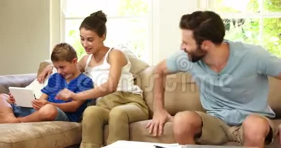可爱的一家人坐在沙发上看着平板电脑视频的预览图