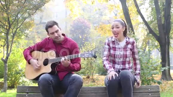 美丽的黑发女人唱歌男人在公园弹吉他视频的预览图