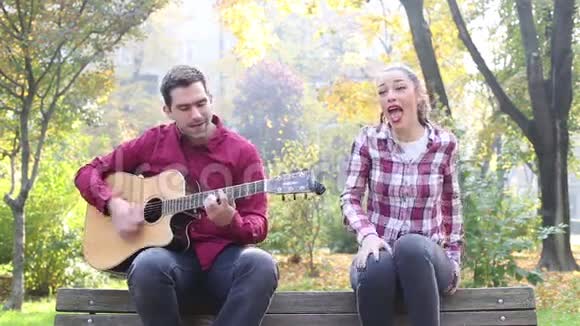美丽的黑发女人唱歌男人在公园弹吉他视频的预览图