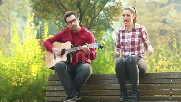 男人一边弹吉他一边和女人一起唱歌一边坐在公园长椅上视频的预览图