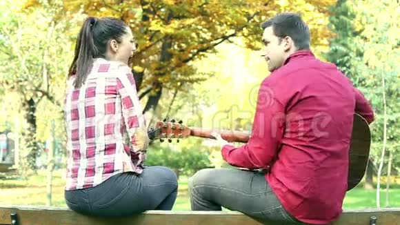 坐在公园长椅上的夫妇男人弹吉他女人唱歌视频的预览图