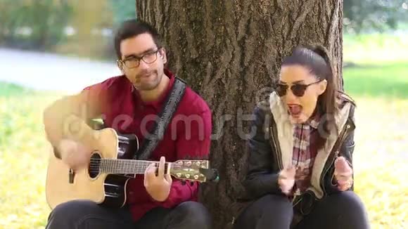 女人唱歌男人弹吉他坐在公园的树上视频的预览图