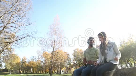 一对年轻的幸福夫妇在公园里用耳机听音乐视频的预览图