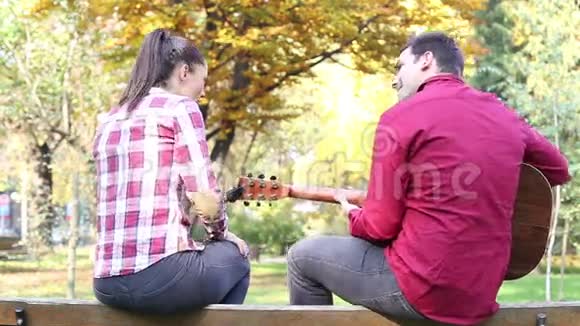 坐在公园长椅上的夫妇男人弹吉他女人唱歌视频的预览图