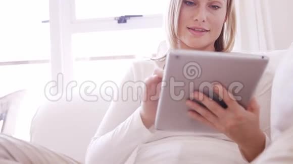 金发女人坐在沙发上用平板电脑视频的预览图