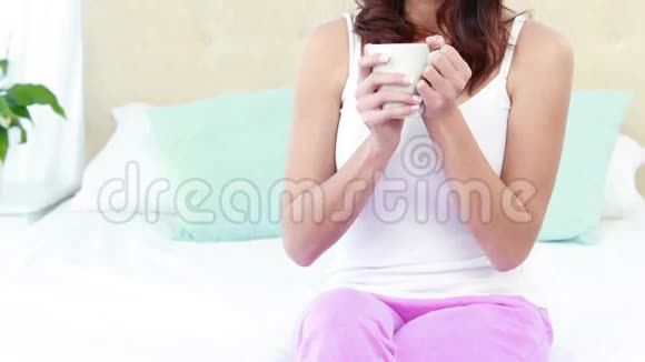 微笑的女人抱着杯子躺在床上视频的预览图