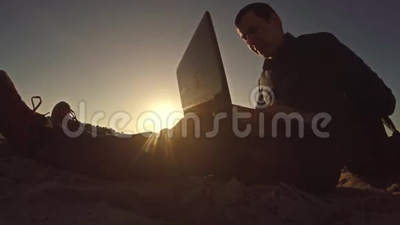一个商人自由职业者在笔记本电脑后面工作坐在沙滩上阳光下自由职业者视频的预览图