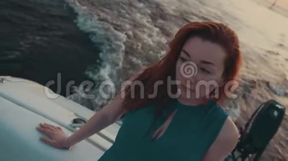 在摩托艇上穿绿松石衣服的红发女孩夏日之夜水视频的预览图