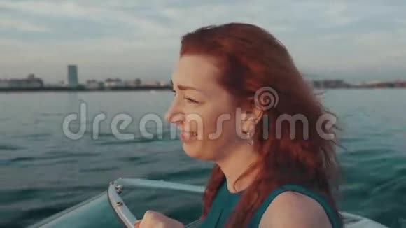 快乐的红发女孩穿着绿松石的裙子在摩托艇上航行美丽的日落视频的预览图