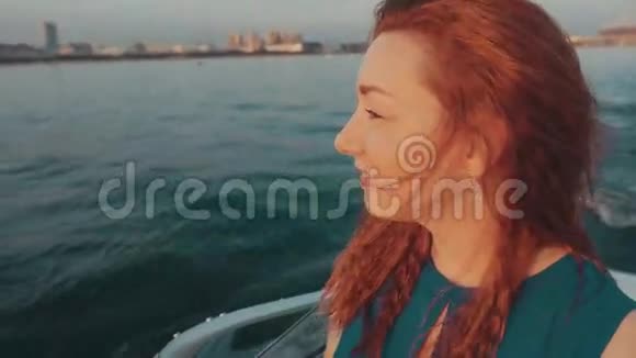 红发女孩穿着绿松石的衣服在摩托艇上航行美丽的日落景观视频的预览图
