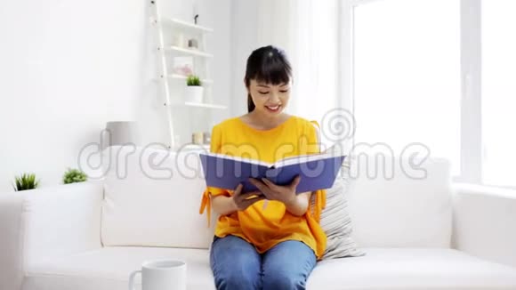 微笑着年轻的亚洲女人在家看书视频的预览图