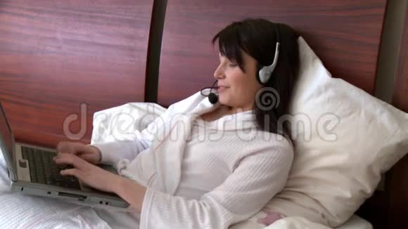 微笑的女人用带有耳机的笔记本电脑视频的预览图