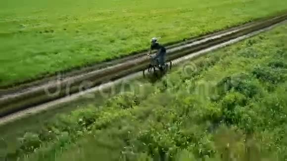 年轻人骑自行车在乡村公路上穿过绿色和黄色的田野视频的预览图