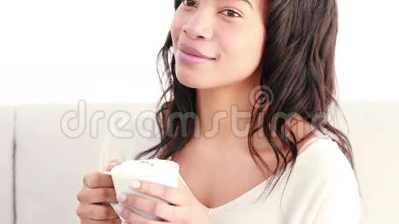 微笑的女人坐在沙发上喝着热饮料视频的预览图