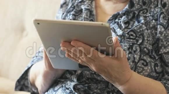 坐在沙发上拿着数码平板电脑的老妇人视频的预览图