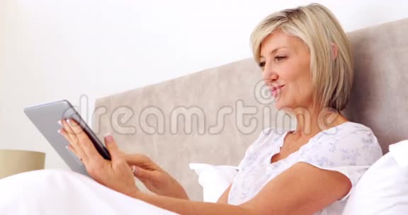 快乐的女人在床上用平板电脑视频的预览图