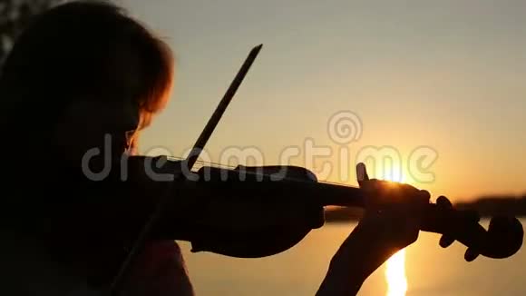 日落时分女小提琴手在湖边拉小提琴视频的预览图