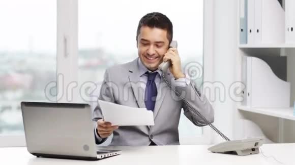 带着笔记本电脑打电话的微笑商人视频的预览图