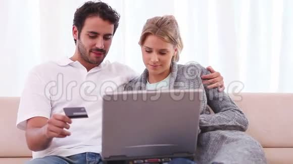 一对夫妇拿着笔记本电脑坐着用信用卡视频的预览图