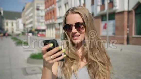 阳光明媚的日子里年轻快乐的女人在城市里用手机发短信视频的预览图