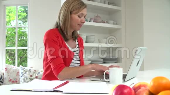在家工作的妇女使用厨房的笔记本电脑视频的预览图