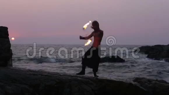 日落时分人类在靠近海洋的悬崖上旋转火坡视频的预览图