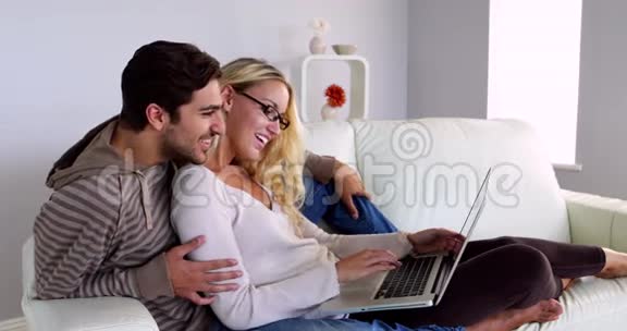 快乐的年轻夫妇用笔记本电脑坐在沙发上视频的预览图