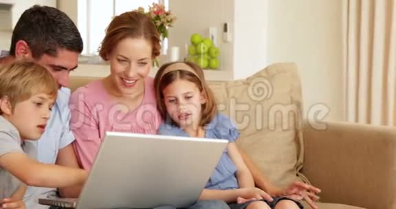 幸福的年轻家庭一起坐在沙发上用笔记本电脑视频的预览图