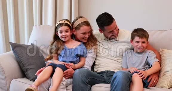幸福的年轻家庭坐在沙发上对着镜头微笑视频的预览图