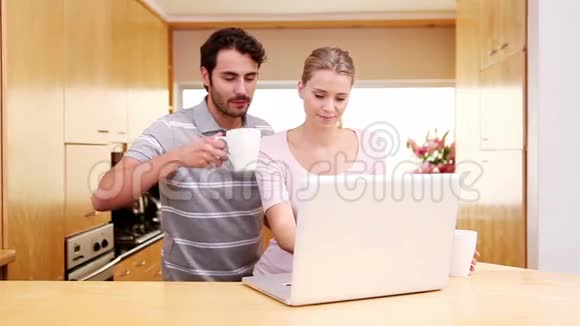 一对微笑的夫妇站着看着笔记本电脑视频的预览图