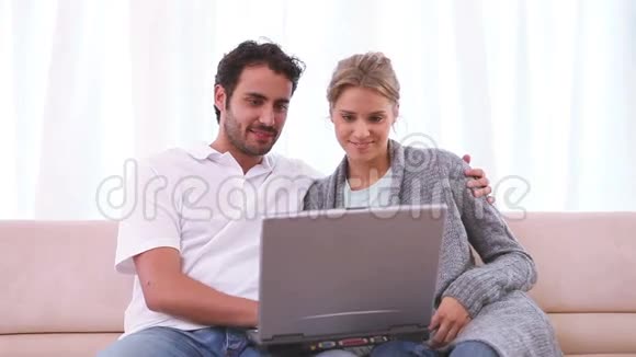 一对夫妇坐在沙发上看着笔记本电脑视频的预览图