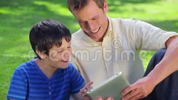 一个微笑的男人和他的儿子用平板电脑视频的预览图