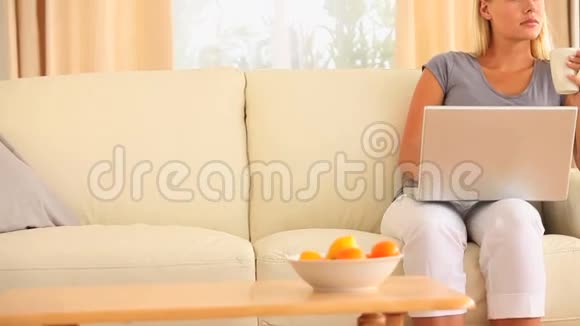 坐在沙发上的女人拿着一杯咖啡和一台笔记本电脑视频的预览图
