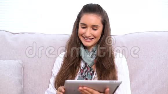 在沙发上用平板电脑微笑的黑发女人视频的预览图