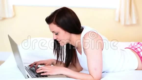 年轻女子躺在床上用她的笔记本电脑视频的预览图
