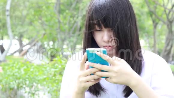 泰国学生十几岁的漂亮女孩用她的智能手机坐在公园里视频的预览图