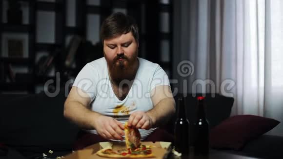 有胡子的胖子在电视机前端着啤酒和爆米花坐在桌子旁吃披萨视频的预览图