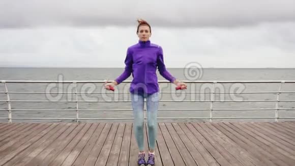 年轻女子在跳绳上锻炼户外运动女孩在海边跳跳绳慢镜头视频的预览图