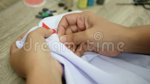 一个女人在白色衬衫上缝一个红色标志时要紧紧抓住她的手视频的预览图