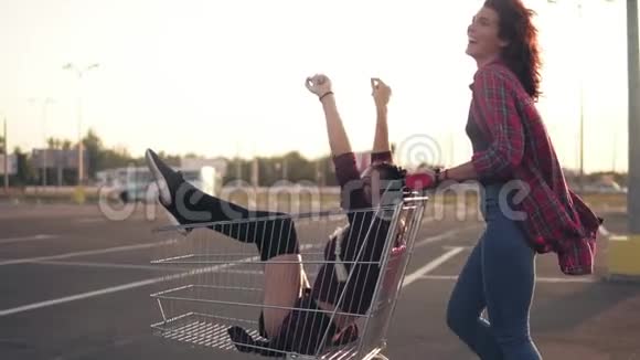 从侧面看一个快乐的年轻女人推着购物车和她的女朋友在购物中心的停车场里视频的预览图