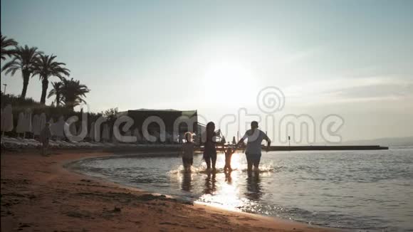 在日落时分活跃的家庭在海滩上玩得开心和享受在一起的剪影视频的预览图