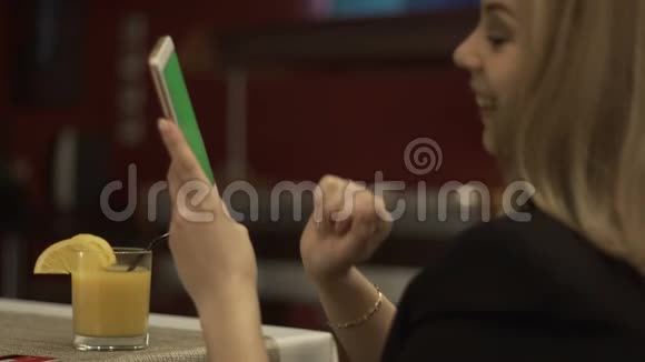 微笑的女人在背景橙汁上触摸绿色屏幕手机视频的预览图