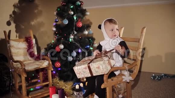 坐在摇椅上的孩子在圣诞树和蜡烛的背景上打开圣诞礼物视频的预览图